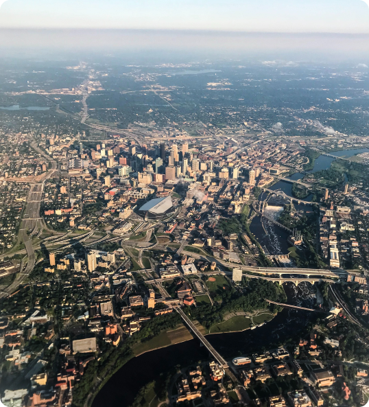 a high altitude photograph of the City of Minneapolis with US Bank Stadium in the center, the Mississippi River cutting through the right side and the suburbs and countryside in the background.