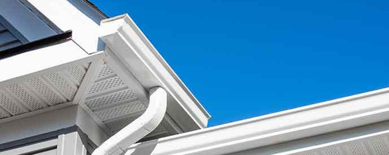looking up at the white soffit, facia and 2 - 6” k-style gutters with downspouts with a perfectly blue sky