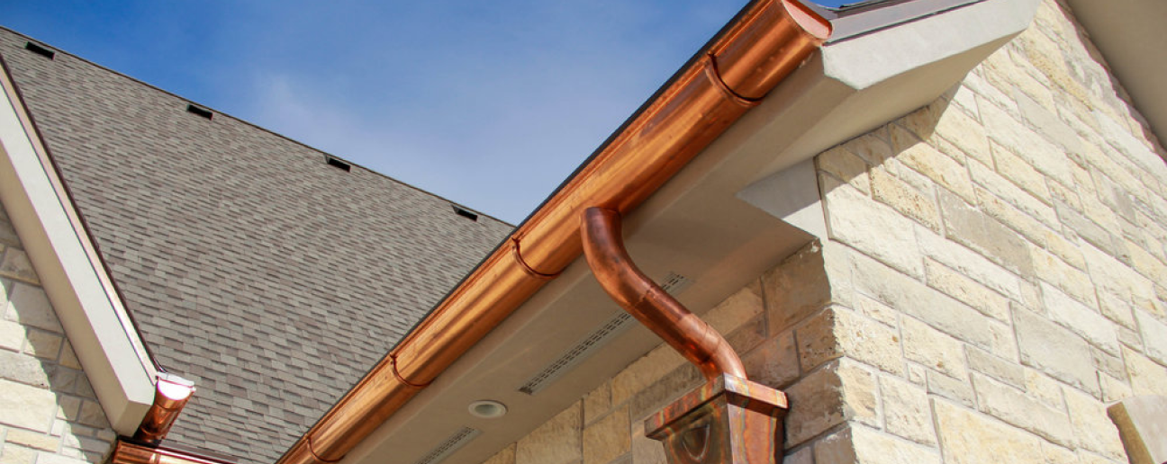 looking up at brand new, shinny copper, half-round gutters and round downspout into a beautiful, rectangular, copper leader head, (open top collection funnel for another downspout).