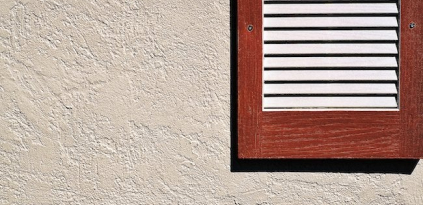 a picture of off white stucco siding and a wood framed window shade