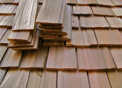 a close-up of newly installed hand split cedar wood shake roofing with a stack of un-installed shakes